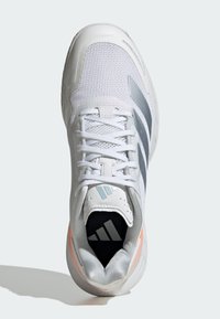 Valkoinen urheilukenkä, jossa on teksturoitu verkkopinta, harmaat raidat ja pehmustettu kaulus. Ominaisuuksia ovat joustava pohja ja vaalean oranssi yksityiskohta.