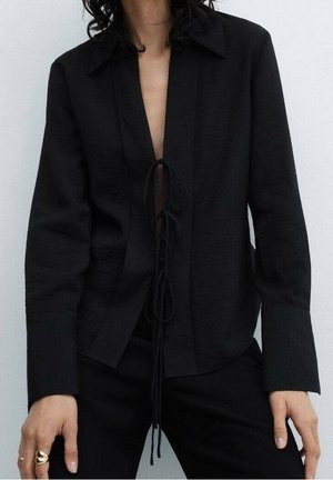 Chemisier en lin noir avec un décolleté en V profond et un lien à l'avant. Présente des manches longues et un col structuré. Texture lisse et design minimaliste.