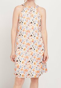 Robe sans manches arrivant au genou avec un col halter et un motif floral aux tons orange, noir et violet sur un tissu blanc.