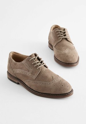 Chaussures habillées en daim marron avec un design à bout ailé, fermeture à lacets, perforations décoratives et une semelle en cuir contrastée cousue.