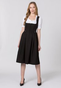 Black dirndl dress with a fitted bodice, square neckline, and vertical seams. Features a flared skirt and buttons. Worn over a white blouse.