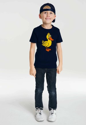 Navy blue T-shirt with a yellow cartoon duck design. The child wears dark jeans and white sneakers, standing confidently.