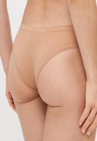 Beige hoge slipjes van glad, rekbaar materiaal. Voorzien van een dunne tailleband en een naadloos ontwerp met minimale stiksels.