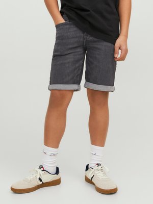 Pantalones cortos de mezclilla gris oscuro con puños enrollados, bolsillos frontales y un ajuste casual. Combinados con calcetines blancos y zapatillas beige.