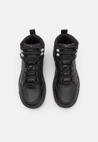 Par de zapatillas altas negras Puma con cuero texturizado, cierre de cordones, ojales metálicos y tiradores sobre un fondo blanco.