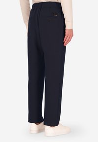 Pantaloni blu navy realizzati in tessuto morbido con vita elasticizzata. Presentano due tasche posteriori con chiusura a bottone. Texture liscia e vestibilità dritta.