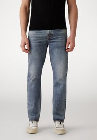 Jeans de mezclilla azul claro con corte recto, desvanecimiento sutil y un diseño clásico de cinco bolsillos. Llevados con zapatillas blancas.