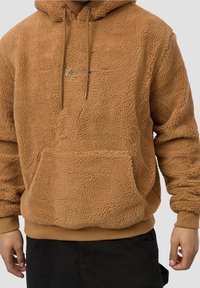 Ruskea fleece-huppari, jossa on teksturoitu pinta, etutasku, kiristysnauhat ja pieni brodeerattu logo rinnassa.