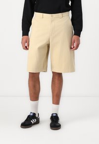 Beige bomuldsshorts med afslappet pasform, to sidelommer og knaplukning, parret med sorte sneakers og hvide sokker.