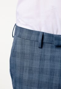 Ljusblå texturerade byxor med ett rutmönster och en platt midja. Tyget har en subtil lyster och en slät yta.