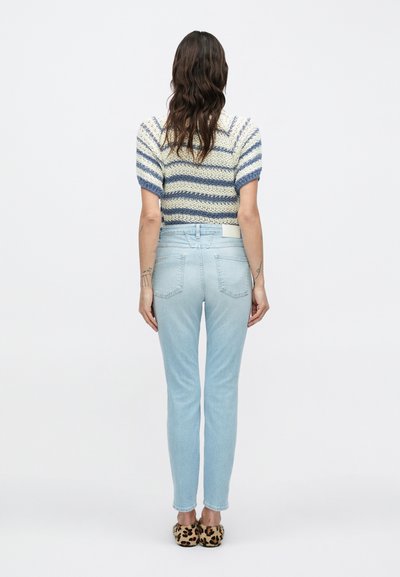 Πλεκτό τοπ με μπλε και κρεμ ρίγες, συνδυασμένο με ανοιχτό μπλε στενά τζιν. Το μοντέλο φοράει παπούτσια slip-on με λεοπάρ σχέδιο.