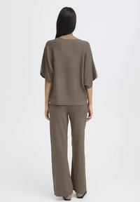 Brauner Strickpullover mit weiten Ärmeln, kombiniert mit passenden, locker sitzenden Hosen. Glatte Textur, minimalistisches Design und entspannte Passform.