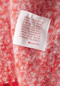 Tessuto rosso e bianco con un aspetto peloso. L'etichetta di cura attaccata mostra un testo motivazionale in rosso su sfondo bianco.