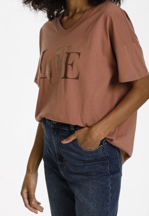 Camiseta de algodón de color rosa, de manga corta y con escote en v, con un gráfico metálico dorado que dice "LOVE", combinada con vaqueros de mezclilla oscuros.