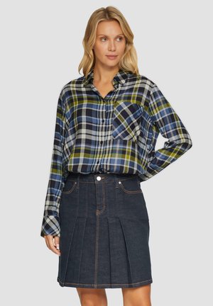Plaid button-up shirt in blue, green, and gray. Paired with a dark denim skirt featuring pleats and visible stitching.