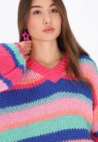 Maglione lavorato a maglia con scollatura a V, caratterizzato da strisce colorate in rosa, blu, verde e pesco. La trama è spessa e consistente. Orecchini a forma di stella.