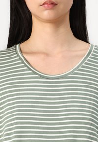 Hellgrünes gestreiftes Oberteil mit rundem Ausschnitt, das abwechselnd dünne weiße Streifen und eine sanfte, glatte Textur aufweist.