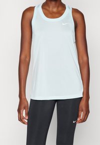 Vaaleansininen urheilutoppi, jossa on pehmeä pinta, syvä kaula-aukko ja kontrastivärinen valkoinen Nike-logo rinnoilla, yhdistettynä mustiin legginsseihin.