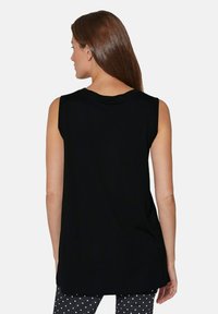 Zwart mouwloos topje met een ronde halslijn, met een losse pasvorm en een zachte textuur. Gecombineerd met een broek met stippenpatroon.