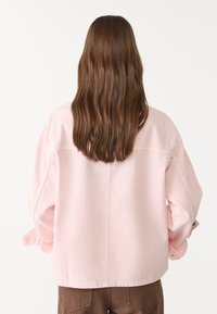 Chaqueta de gran tamaño en rosa claro con una textura suave, costuras doblemente cosidas y acentos de botones en las mangas. Diseño simple y limpio.