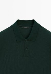 Donkergroene polo met een gestructureerde stof, voorzien van een klassieke kraag, drie knopen en een labeltag bij de halslijn.