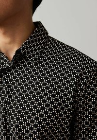 Maglietta nera a maniche corte con un motivo geometrico bianco, dotata di colletto e dettagli con bottoni, realizzata in tessuto leggero.