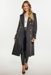 Czarny trenchcoat o dopasowanym kroju, z dużym kołnierzem, podwójnymi guzikami i rękawami na pasek, w połączeniu ze skórzanymi legginsami i szpilkami.
