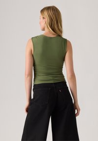 Olive green sleeveless top with a fitted design, showcasing a smooth, stretchy fabric; paired with wide-leg black denim jeans.