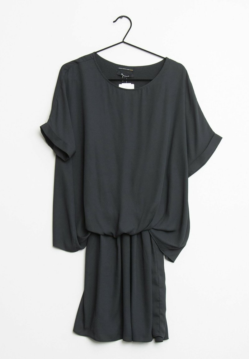 Robe noire à manches courtes et coupe ample avec un détail froncé à la taille, suspendue sur un cintre noir contre un fond blanc.