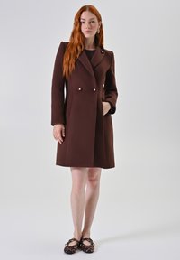 Bruine double-breasted jas gemaakt van gestructureerde stof, met twee knopen en een zijzak, gecombineerd met vlakke schoenen met luipaardprint.