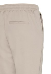 Pantalon beige à taille élastique, poche arrière passepoilée et poche couture côté, vu de dos et de côté. Aucune personne présente.