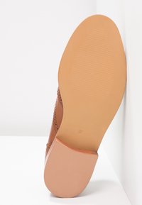 Chaussure en cuir marron avec un design perforé, un petit talon et une semelle en caoutchouc texturée. Taille 37 marquée sur la semelle.
