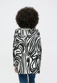 Μαύρο και άσπρο πουκάμισο με διακοσμητικά σχέδια, με γιακά και μακριά μανίκια, κατασκευασμένο από ομαλό ύφασμα.