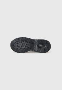 Black athletic shoe sole with textured rubber, featuring a pattern of grooves and shapes for grip and traction. Circular heel detail included.