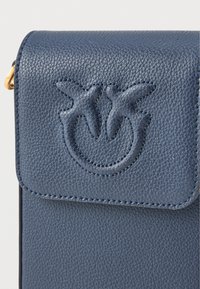 Tmavě modrá kožená crossbody taška s texturovaným povrchem, klopovým zavíráním, vytlačeným logem a zlatými kovovými akcenty.