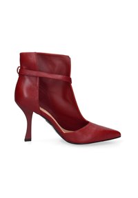 Stivaletto in pelle rossa con punta affusolata, lati aperti, sottile cinturino alla caviglia e tacco a stiletto. Texture liscia e design minimalista.