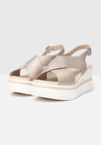 Sandali platform metallici beige con cinghie incrociate e fibbia regolabile alla caviglia; suola bianca spessa con un sottile design a strati.