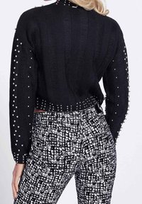 Czarny dziergany krótki sweter z teksturowanym wzorem i ozdobnymi ćwiekami na rękawach. Połączony z wysokim stanem spodni w czarno-biały wzór.