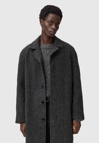 Grå uldblandingsfrakke med knaplukning, slå-om krave og afslappet pasform. Båret over en struktureret grå striktrøje med et subtilt mønster.