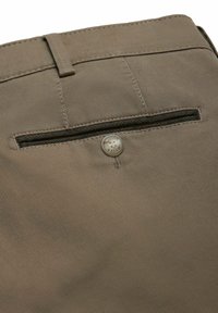 Close-up van een bruine, gestructureerde stoffen broekzak met een enkele knoopsluiting en een riemlus erboven.