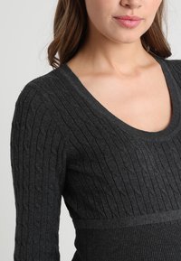 Czarny sweter o prążkowanej fakturze, z głębokim dekoltem w kształcie litery V i dopasowanym krojem, z kontrastującym paskiem w talii dla podkreślenia sylwetki.