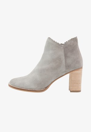 Bottine grise en daim avec un bord festonné, un bout arrondi et un talon empilé texturé de couleur brun clair. Présente des détails cousus.