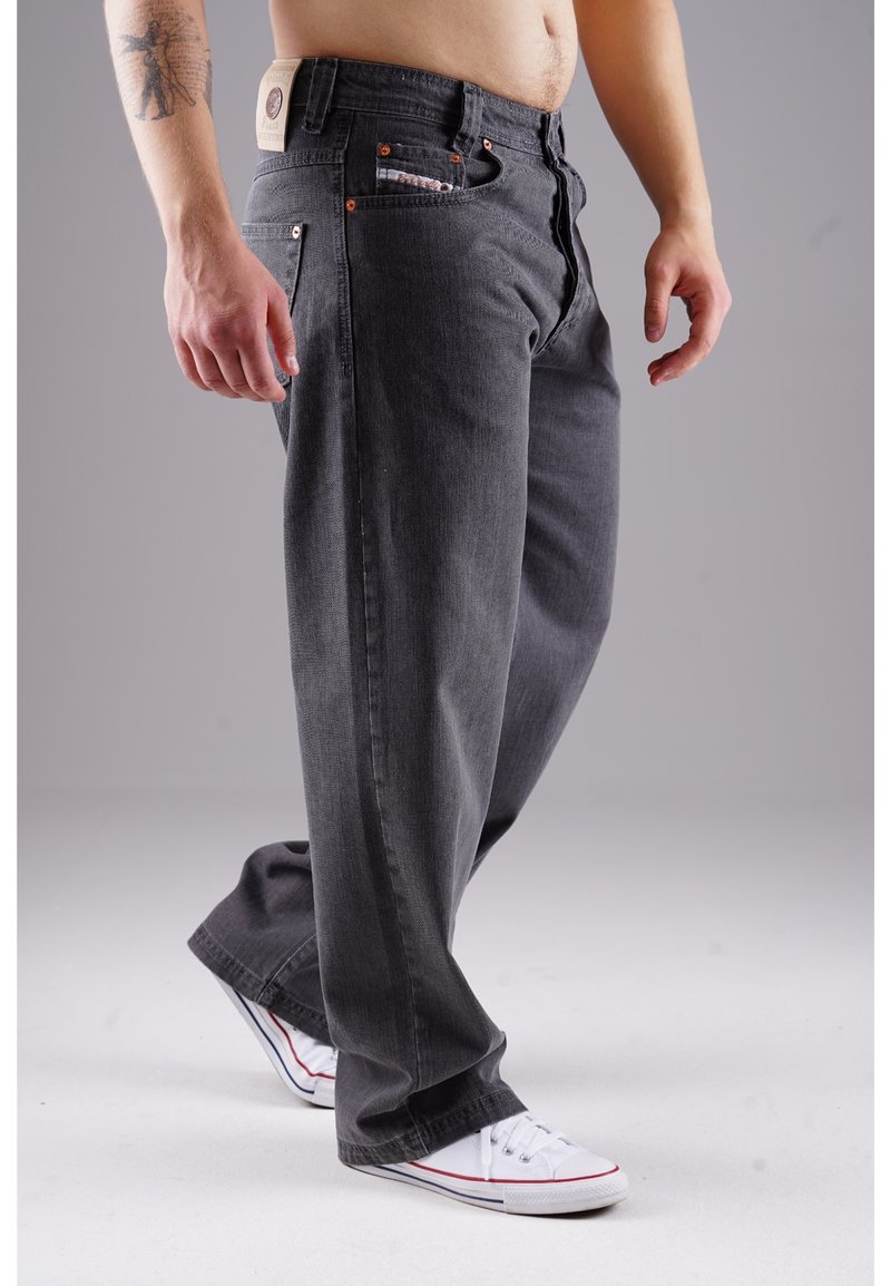Gray denim jeans with straight legs, five pockets, copper hardware, and a back patch. Worn with white sneakers featuring red accents.