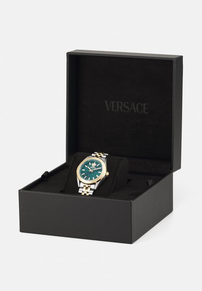 Versace kell mustas karbis. Omab türkiissinist nägu, kuldseid aktsente, hõbe-kuldtoonilist rihma, julgeid tunni numbreid ja logo kell 12 kohal.