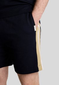 Pantaloni corti blu navy con tasche laterali, impreziositi da strisce crema e beige lungo il lato. Realizzati in tessuto morbido con una vestibilità comoda.