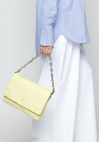 Borsa a tracolla in pelle gialla con una catena, caratterizzata da una texture liscia, chiusura a pattina e dettaglio del logo in rilievo sul davanti.