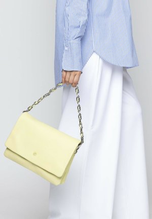 Sac à main en cuir jaune avec une anse en chaîne, présentant une texture lisse, une fermeture rabat et un détail de logo embossé sur le devant.