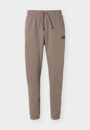 Pantaloni della tuta color talpa con cintura elastica, coulisse e polsini, con una piccola etichetta del marchio nera sulla coscia destra.