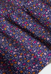 Tissu bleu marine avec un petit motif floral en rose, orange, rouge et vert, froncé avec des coutures visibles créant des plis et de la texture.