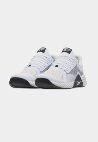 Ζεύγος λευκών και μαύρων αθλητικών παπουτσιών Reebok με πλέγμα στο πάνω μέρος και παχιές υφασμάτινες σόλες, απεικονίζεται από μπροστινή γωνία σε λευκό φόντο.